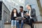 Confident international co workers sitting on wooden bench in front of office and discuss results of joint work.