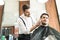 Confident Male Barber Styling Client`s Beard In Shop