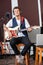 Confident Man Playing Guitar While Sitting On Stool