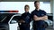 Confident man and woman police officers standing near patrol car crossing hands