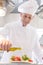 Confident mature chef using pouring oil on salad in plate at restaurant