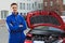 Confident mechanic with arms crossed standing by car