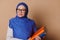 Confident Middle-Eastern Muslim woman teacher educator at high school with a stack of book, isolated on beige background