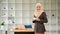 A confident Muslim businesswoman stands in her modern office with a coffee cup in her hands