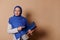 Confident Muslim woman in hijab, carries pile of books, looking at camera, isolated on beige background. World book Day.