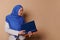 Confident Muslim woman in hijab, smiling, holding a pile of hardcover books in her hands, isolated on beige background