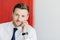 Confident office worker in white shirt with tie, hand on cheek, contemplates new stage in life. Poses against red and white