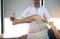 Confident physical therapist helps patient use resistance band stretching out his leg in clinic room