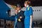 Confident pilot in uniform and aviator sunglasses walking together with two air stewardesses in blue uniform in front of