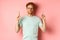 Confident and pleased young man with red hair, wearing glasses and t-shirt, pointing fingers up and smiling with smug