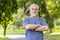 Confident senior man with arms crossed standing in lush park