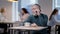 Confident senior man talking on the phone sitting in restaurant or cafe with blurred people resting at background