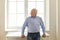 Confident serious senior man standing near the window in new house and looking away