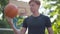 Confident smiling man playing ball with basketball ring at the background. Portrait of redhead Caucasian sportsman