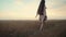 Confident smiling young european woman in light dress walking alone along yellow wheat barley field at sunset