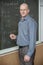 Confident teacher standing by blackboard with formulas