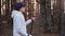 Confident woman in cap and glasses exercising scandinavian walk in forest. Medium shot on RED camera