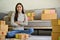 Confident young Asian female small business owner sits in her living room with shipping boxes