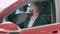 Confident young bearded businessman in Covid-19 face mask sitting on driver\'s seat in red car examining vehicle