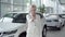 Confident young blond woman showing car keys at camera and smiling. Businesswoman in white suit buying vehicle in