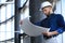 Confident young businessman in hardhat holding blueprint and inspecting it while standing indoors