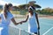 Confident young female biracial players doing handshake over net at tennis court on sunny day