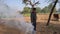 Confident young guy cleaning grass heap in field. Stubble burning with deep fog smoke