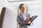 Confident young saleswoman writing on document while standing in apartment