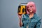 Confident young woman with pink hair and sunglasses posing with yellow old boombox in a shoulder isolated on grey wall background
