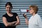 The conflict of generations. An old woman yells into a megaphone at her middle-aged daughter against gray background