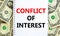 Conflict of interest symbol. Words `Conflict of interest` on white note. Beautiful background from dollar bills. Business,