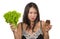 Confused Asian Korean woman holding delicious and tempting chocolate cupcake and healthy green lettuce struggling choice low