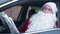 Confused bearded Santa Clause sitting in car on driver's seat examining paper map. Portrait of lost Father Christmas in
