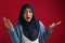 Confused beautiful Asian muslim woman wearing hijab, spreads hands sideways, smirks face, shocked to be accused