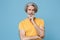 Confused elderly gray-haired mustache bearded man in casual yellow t-shirt posing isolated on blue background studio