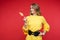 Confused girl in yellow dress with belt looking at lollipop.