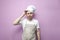 Confused guy cook in an apron scratches his head with his hand and thinks on a pink background