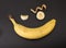 Confused, laughing, curious evil smiling face made of banana with black background. Fruit emoji creative concept.