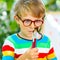 Confused little kid boy with glasses holding watercolors and brushes. Happy child and student is back to school