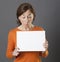 Confused middle aged woman holding white communication panel, grey background