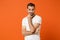 Confused pensive young man in casual white t-shirt posing isolated on orange wall background, studio portrait. People