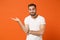 Confused puzzled young man in casual white t-shirt posing isolated on bright orange wall background, studio portrait