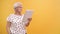 Confused senior lady holding gift tablet looking around for a help. Isolated on orange background