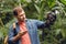 Confused traveler with backpack pointing at gas mask in tropical forest.