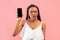 Confused young black woman showing mobile phone with blank screen on pink studio background, mockup