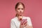 Confused young redhead woman holding pink smartphone.Embarassed girl has problem with broken not working mobile phone