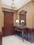 Console key table with mirror in wooden frame and table lamp. Classic hallway interior with patterned yellow wallpaper and brown