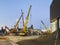 Construction of a broken bridge on a busy road. huge, yellow, metal cranes carry concrete blocks and beams for the construction of