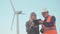 Construction business. Business lady and young man in helmet and reflective vest on windmills background using digital