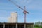 A construction crane turns an arrow. The boom of a crane with a hook on a long cable carries buckets. Blue sky, high-rise building